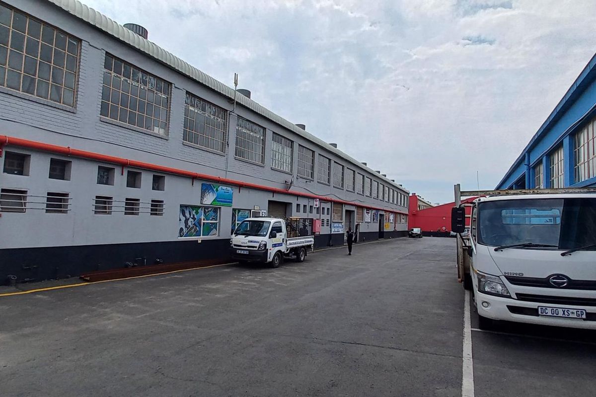 Exterior view of an industrial warehouse facility featuring a large asphalt yard, steel-framed windows, and exposed fire safety infrastructure.
