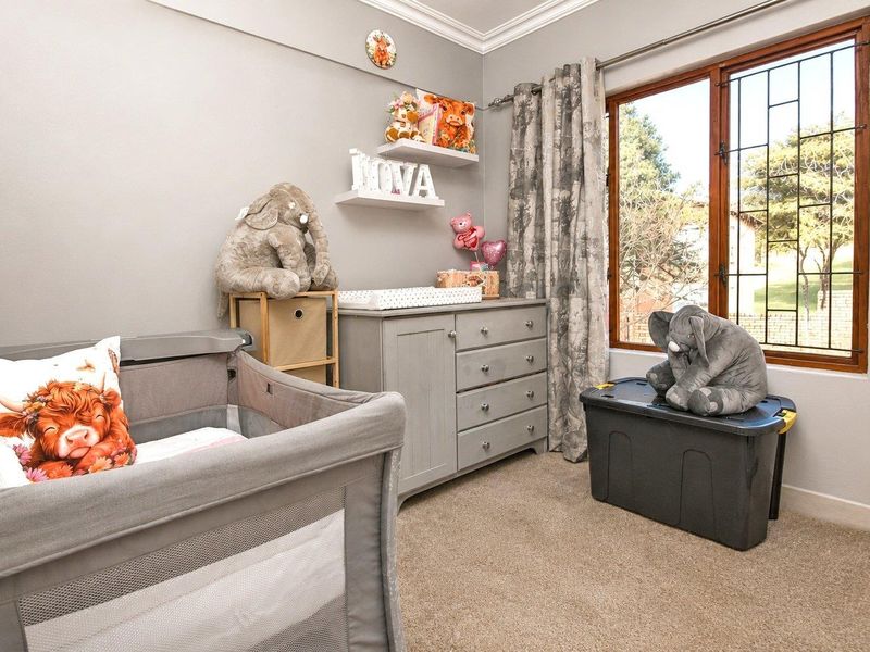 A cozy bedroom featuring carpeted flooring, decorative cornicing, and a timber-framed window with security bars, offering a functional space for a nursery.