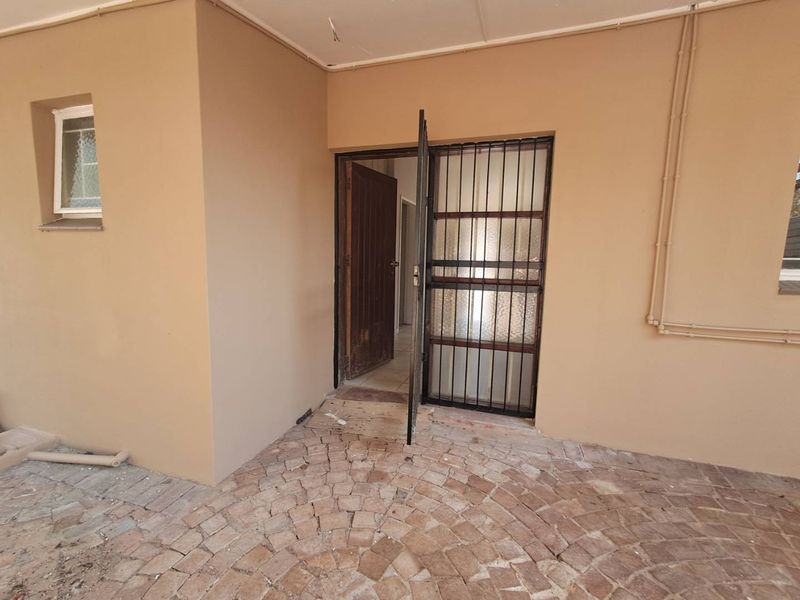 A covered patio area featuring paved flooring, a security gate, and external access to the main dwelling.