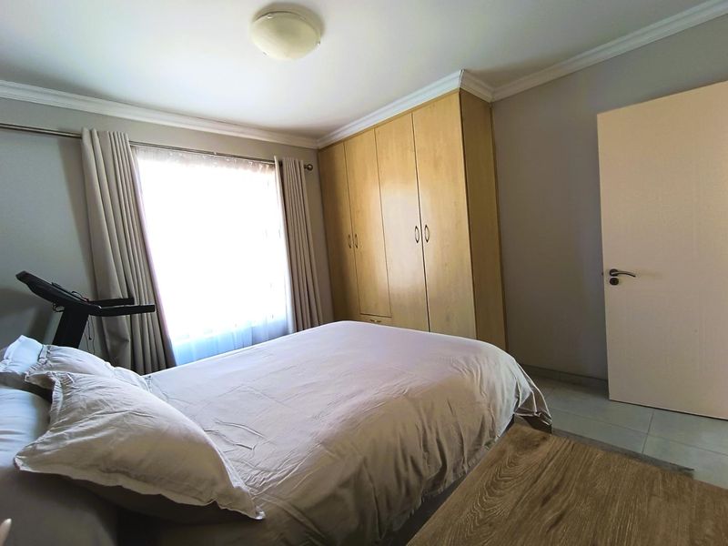 A functional bedroom featuring built-in wooden cupboards, tiled flooring, and neutral wall finishes, providing a practical and comfortable living space.