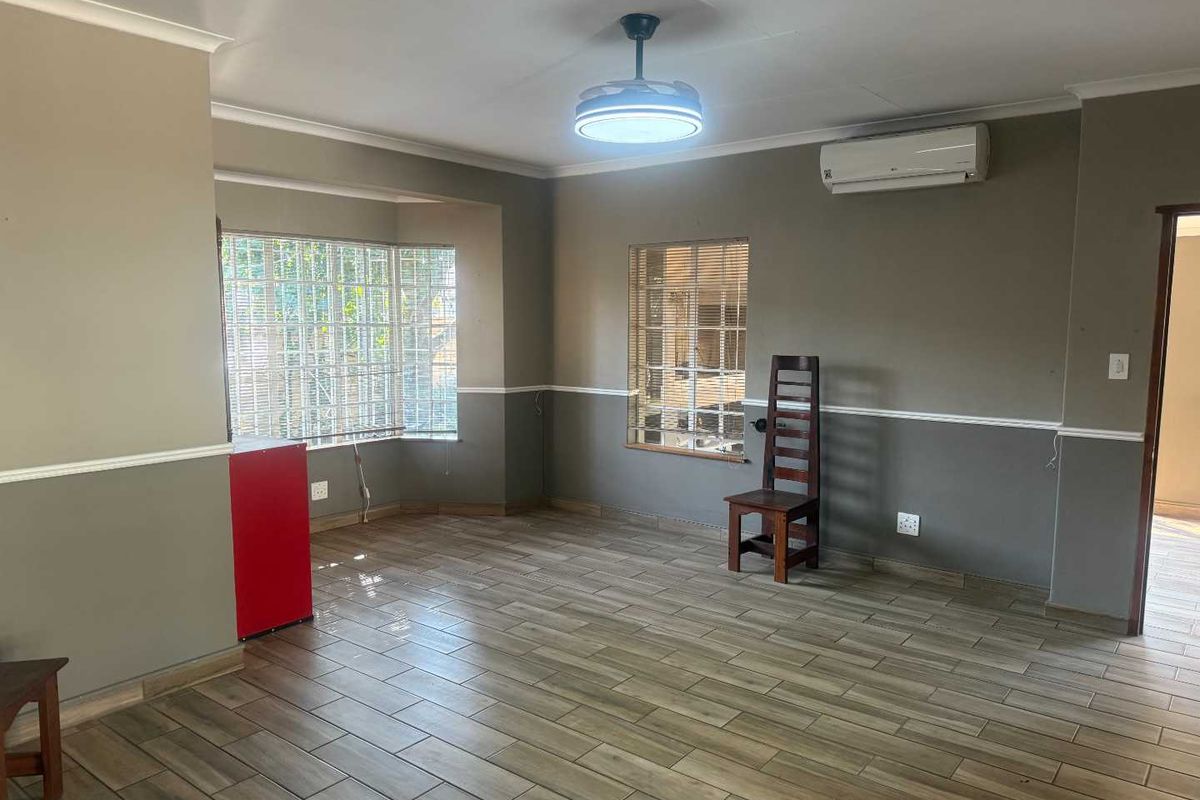 Spacious living area featuring wood-look tiled flooring, a ceiling fan, air conditioning, and a bay window with security bars.