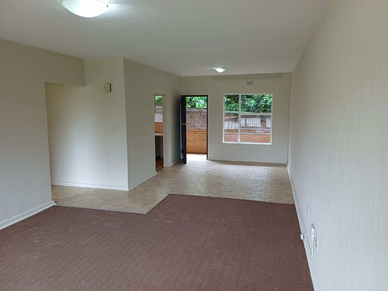 An open-plan living area featuring a combination of carpeted and tiled flooring, neutral walls, and direct access to an outdoor space.