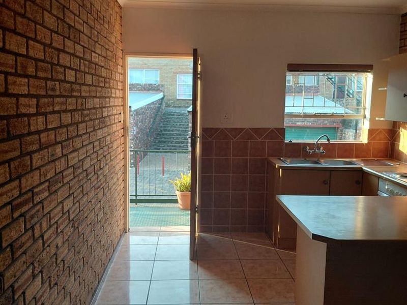 A functional kitchen featuring exposed brick walls, tiled flooring, and built-in cabinetry with direct access to an outdoor balcony area.