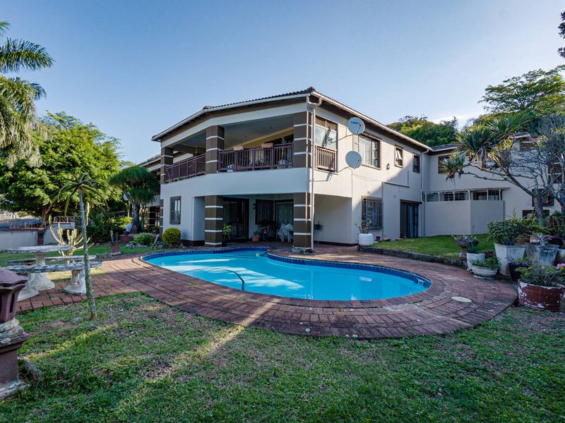 Rear view of the property featuring a swimming pool, paved surround, and a covered balcony overlooking the garden.