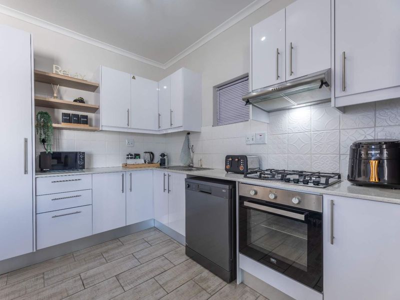 Modern kitchen featuring white gloss cabinetry, stone countertops, gas hob, built-in oven, extractor fan, and tiled backsplash with wood-look floor tiles.