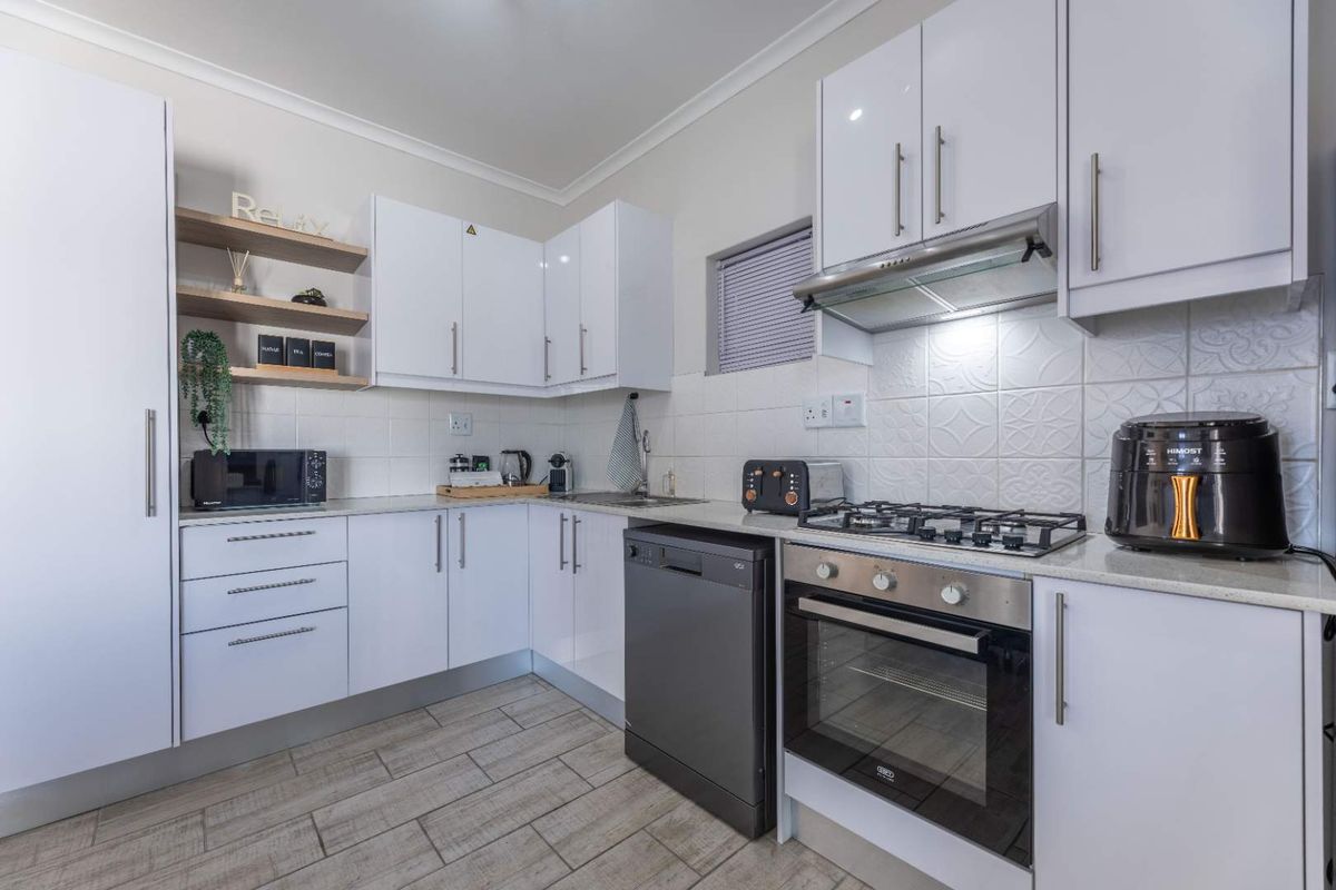 Modern kitchen featuring white gloss cabinetry, stone countertops, gas hob, built-in oven, extractor fan, and tiled backsplash with wood-look floor tiles.
