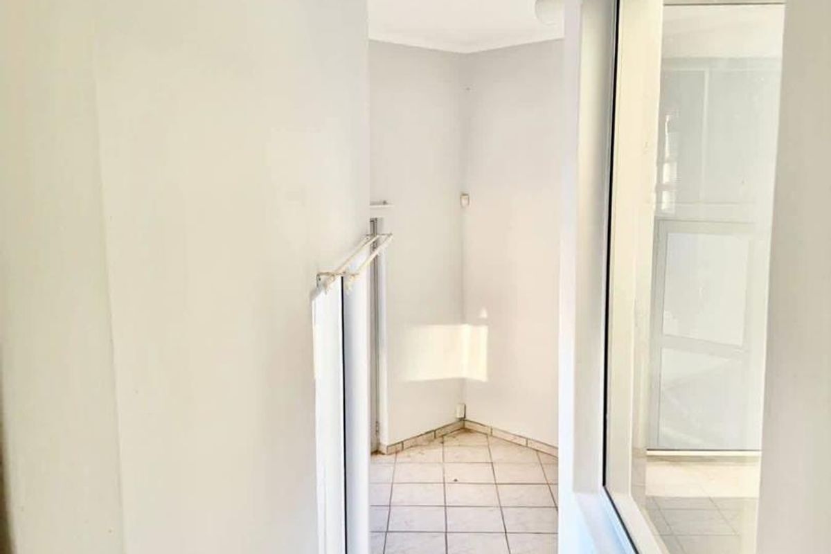 A narrow, tiled hallway or transition space featuring large windows that provide natural light and a view into adjacent areas.