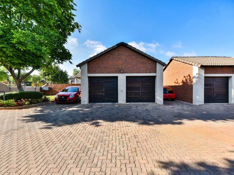 Exterior view of a townhouse complex featuring brick-faced double garages with sectional doors and a paved driveway.