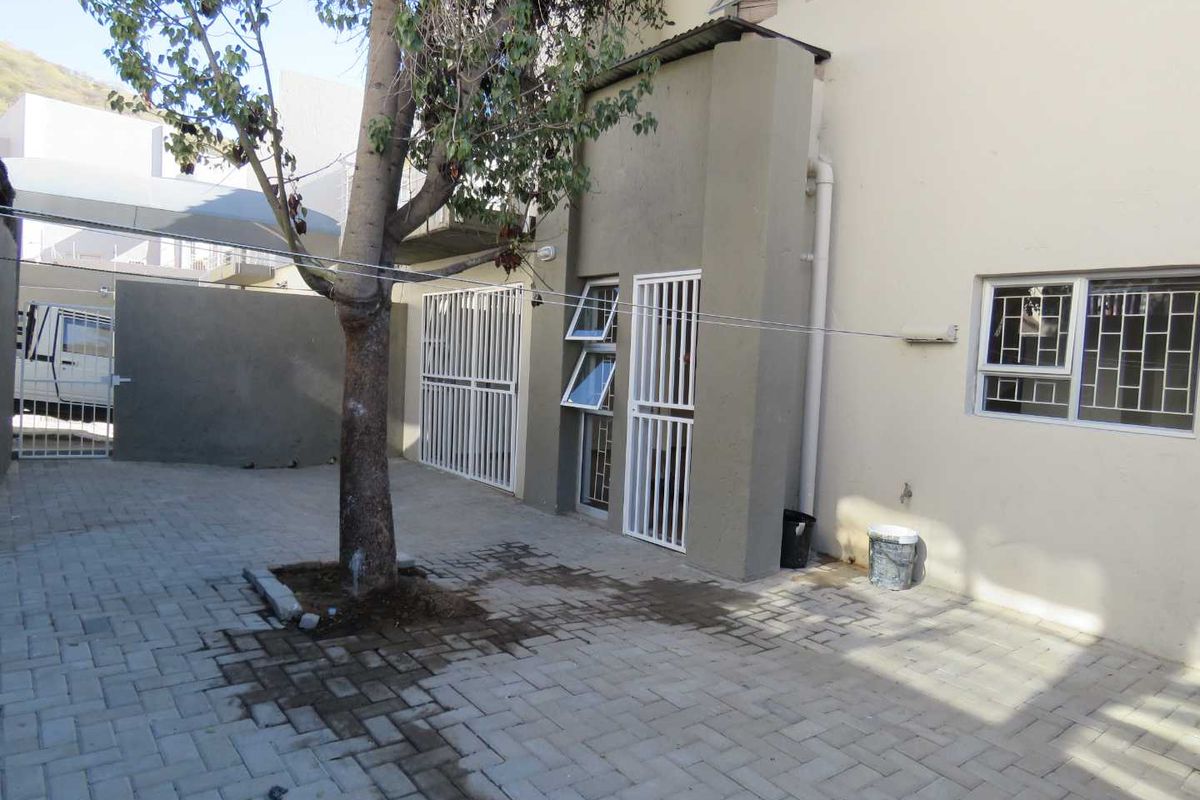 A paved rear courtyard area featuring security gates, window security bars, and a mature tree, providing a functional outdoor space for the townhouse.
