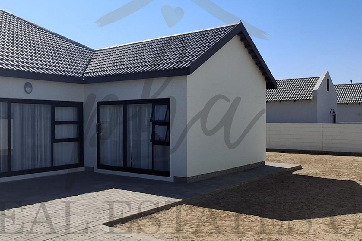 Rear view of the property featuring a paved patio area, modern sliding doors, and a tiled roof, set against a clear sky.