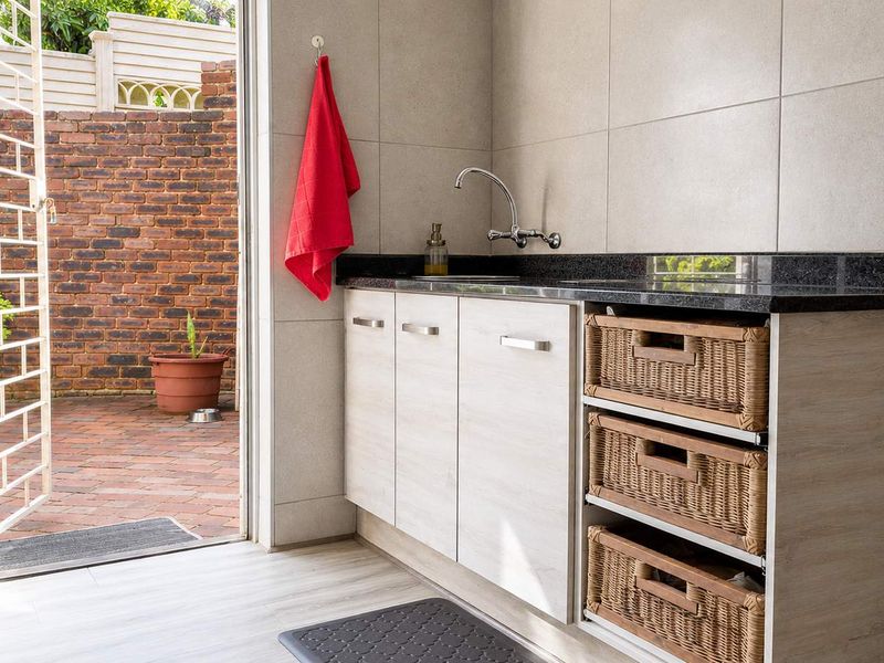 A functional laundry area featuring built-in cabinetry, granite countertops, a sink, and direct access to an outdoor brick-paved courtyard.