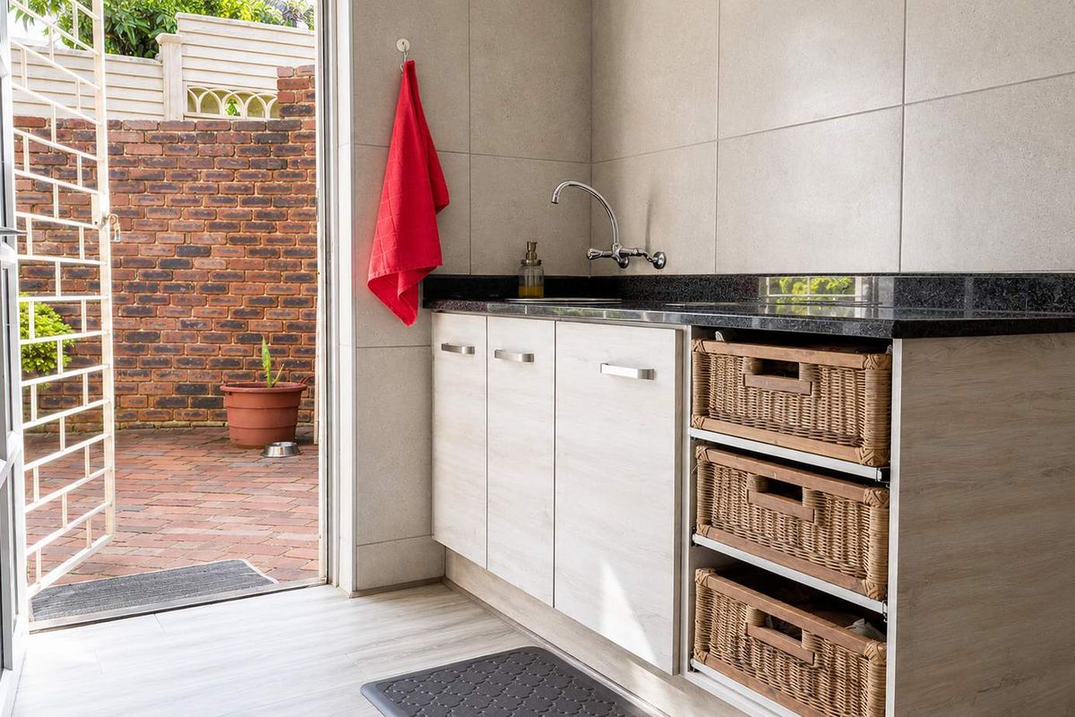 A functional laundry area featuring built-in cabinetry, granite countertops, a sink, and direct access to an outdoor brick-paved courtyard.