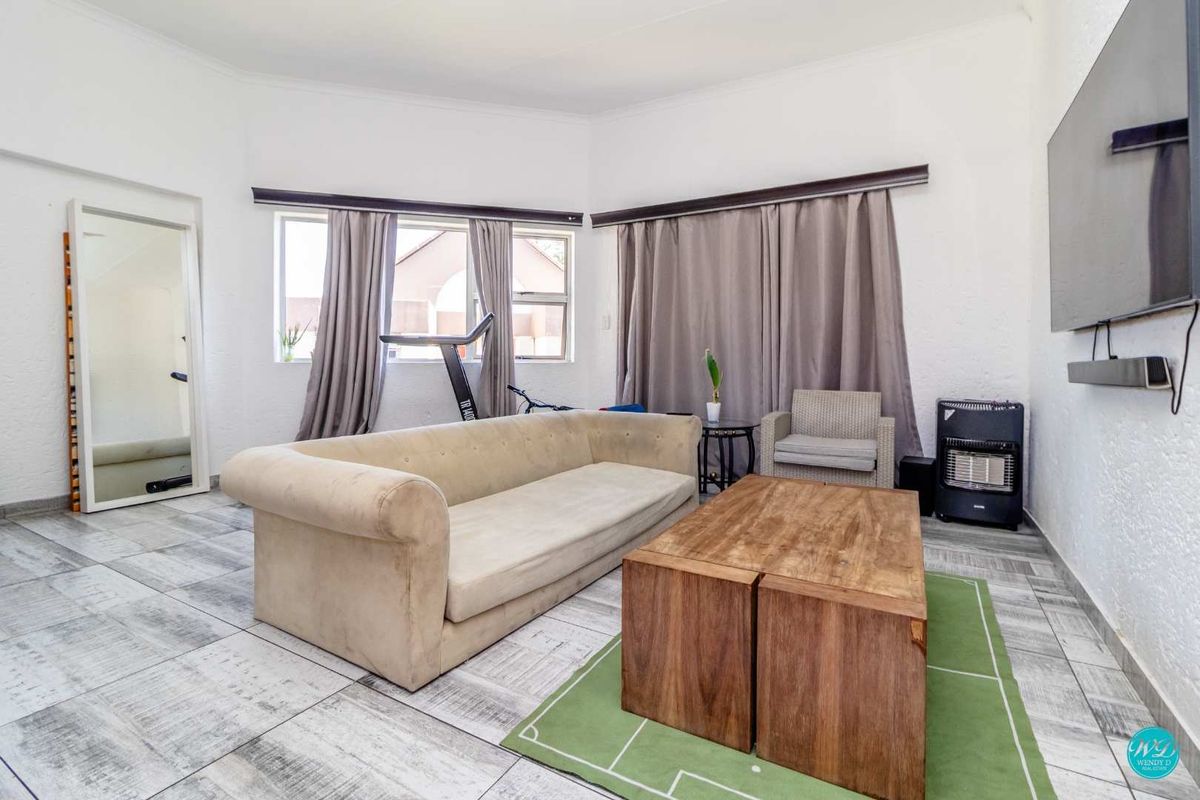 A spacious living room featuring tiled flooring and large windows, providing a bright and functional area for relaxation.