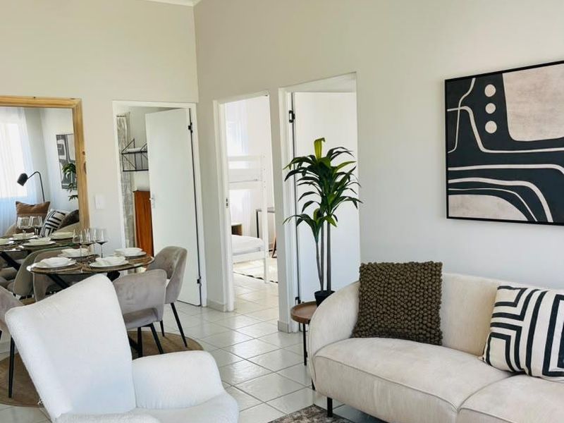 A bright and airy living room featuring tiled flooring, a vaulted ceiling, and neutral wall finishes, providing a comfortable and well-maintained living space.