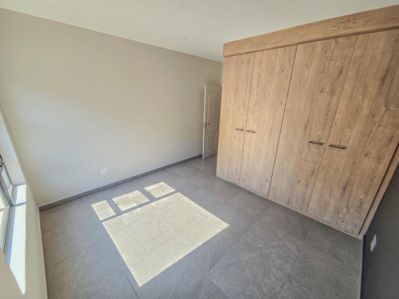 A bright, empty bedroom featuring modern grey floor tiles and large, wood-finish built-in cupboards.
