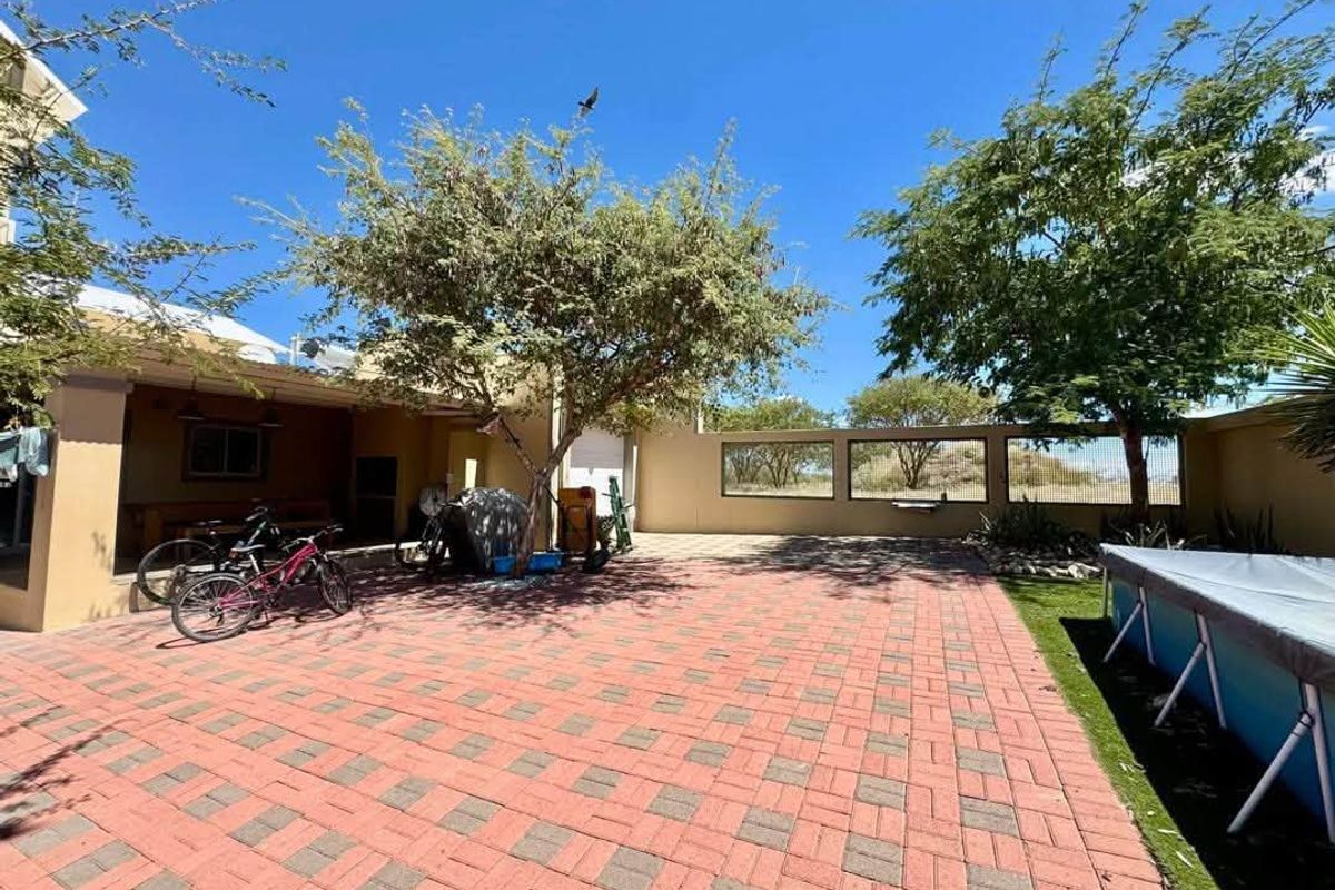 A spacious rear exterior area featuring a paved patio, a covered entertainment space with a built-in braai, and a secure boundary wall.