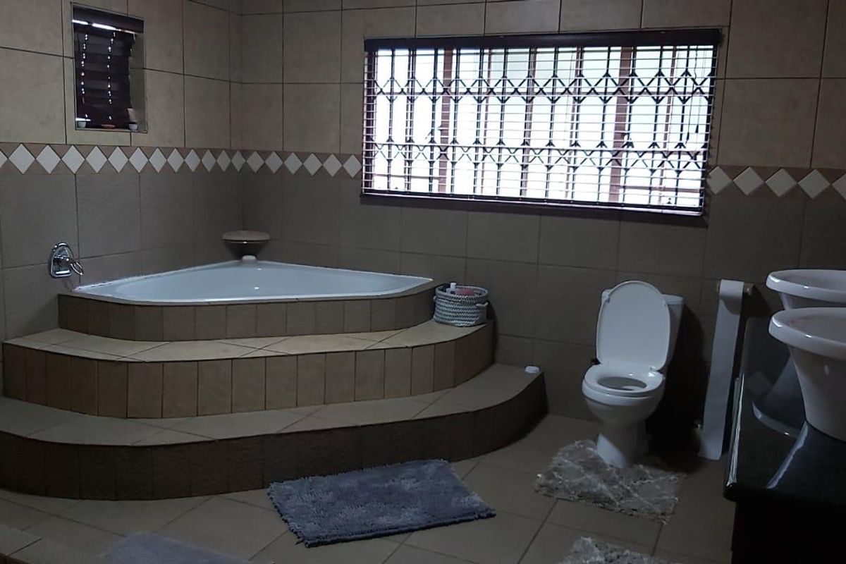 A spacious bathroom featuring a raised corner bathtub, dual vessel sinks on a vanity, and a toilet, finished with neutral wall and floor tiling.