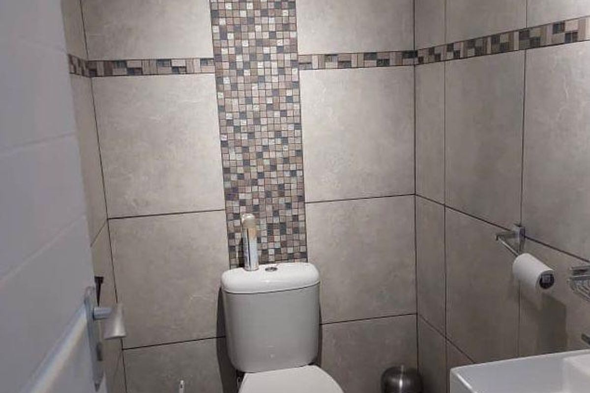 A compact guest bathroom featuring modern floor-to-ceiling tiling with a decorative mosaic accent strip, a white toilet, and a wall-mounted vanity basin.