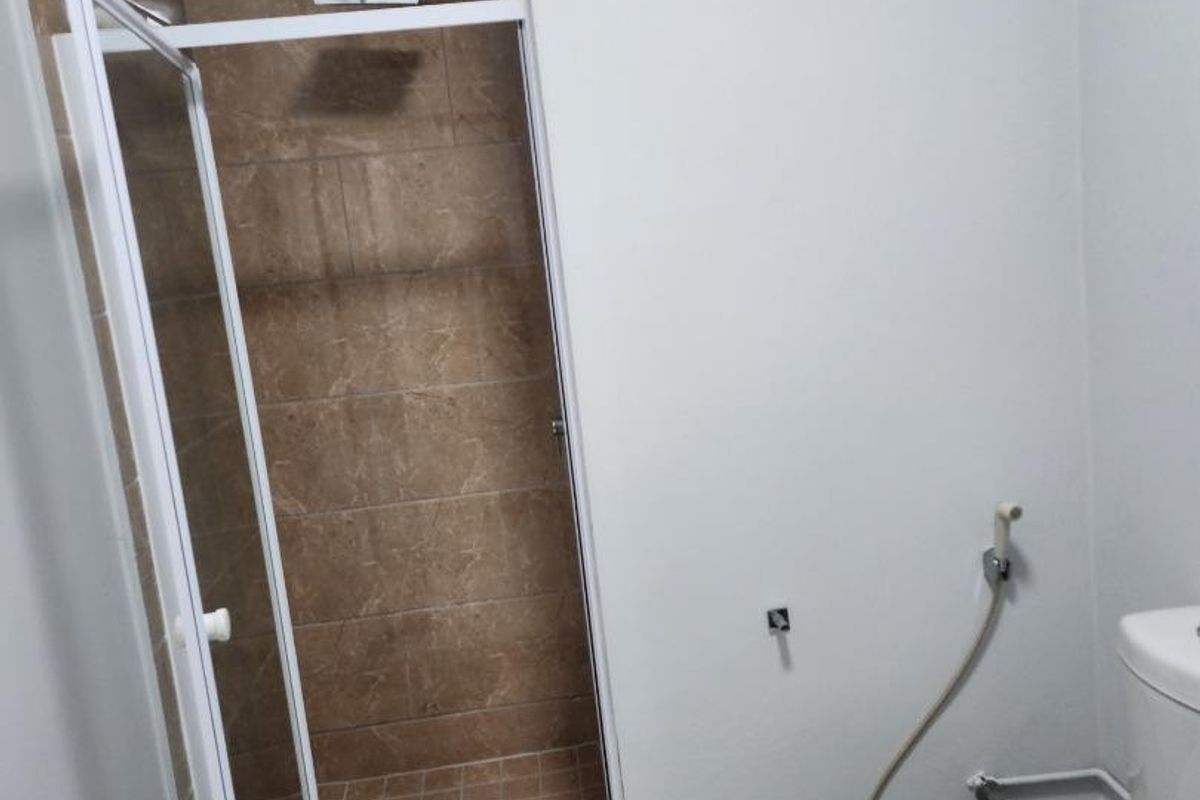 A clean, functional bathroom featuring a tiled shower enclosure with a glass door, a standard toilet, and a bidet spray attachment.