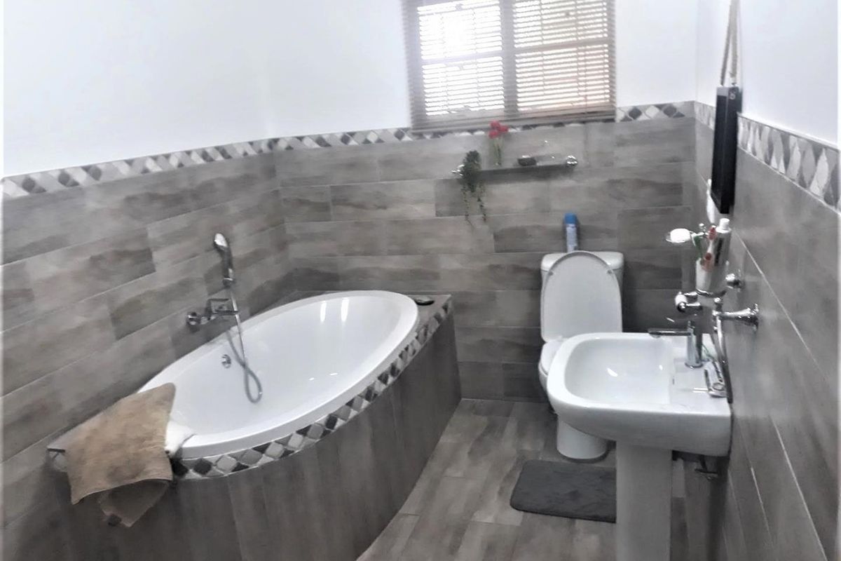 A functional bathroom featuring a built-in bathtub with shower mixer, pedestal basin, and toilet, finished with wood-look wall and floor tiling.
