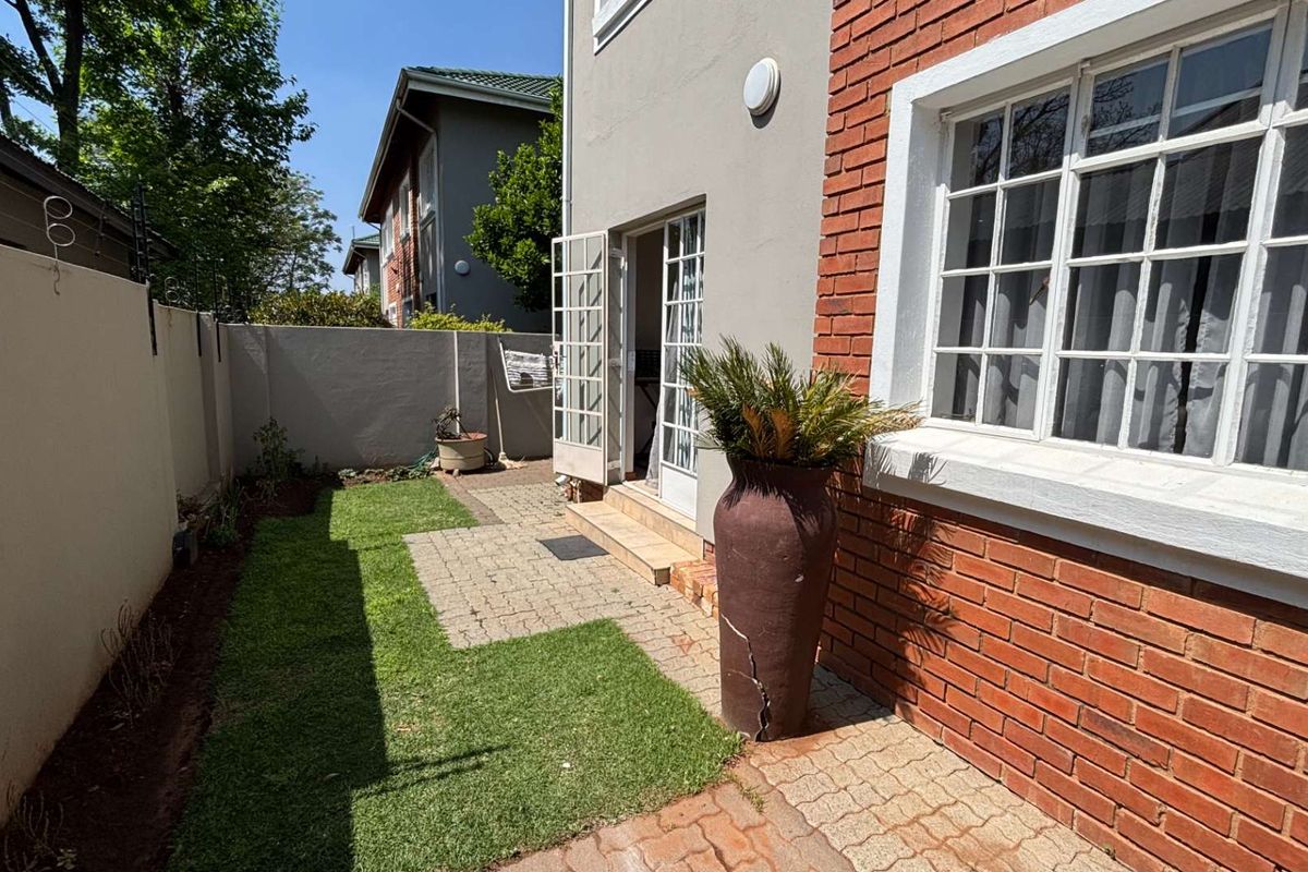 A private rear garden featuring a paved patio area, small lawn, and brick-accented exterior wall with classic grid-style windows and french door access.