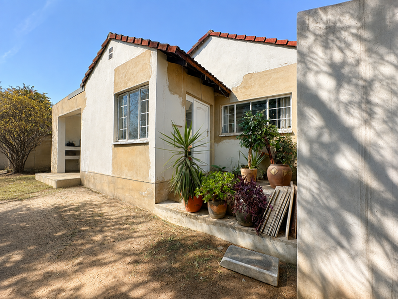 Rear exterior view of the house featuring a concrete patio, built-in outdoor braai area, and terracotta roof tiles with visible wear to the wall finishes.