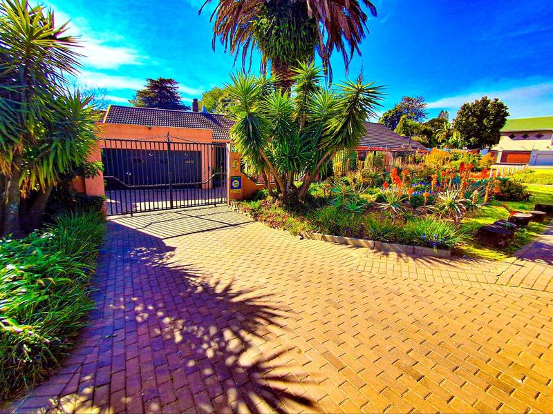 Front exterior view of the property featuring a paved driveway, secure metal gate, and established garden landscaping.