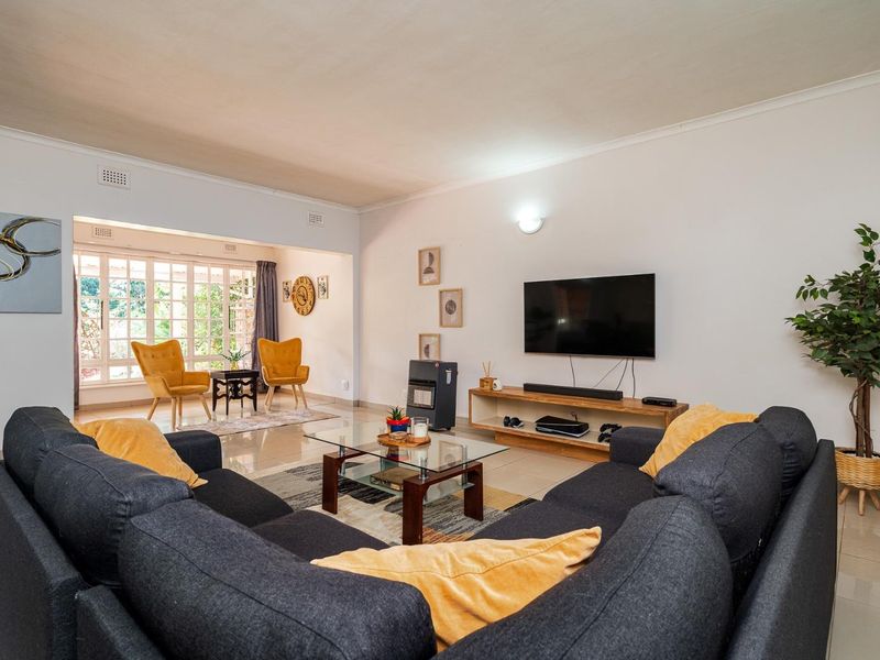 Spacious open-plan living area featuring neutral tiled flooring, cove cornicing, and large windows that provide ample natural light.