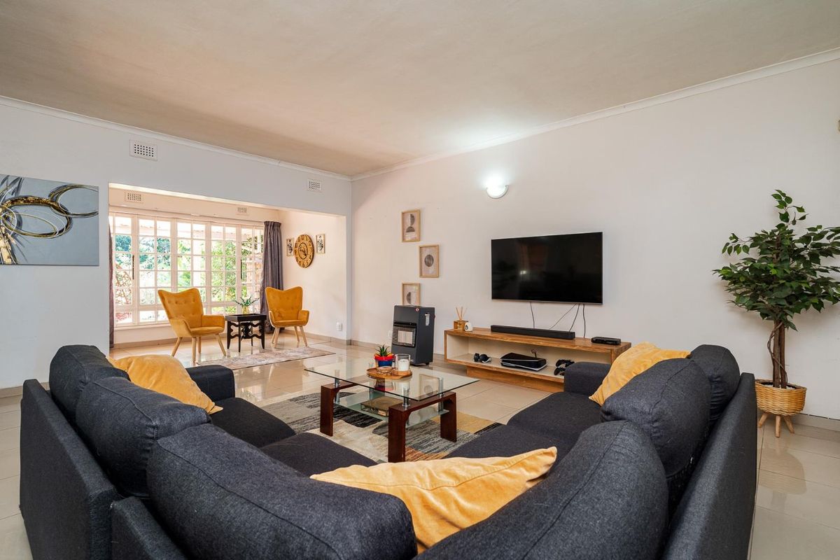 Spacious open-plan living area featuring neutral tiled flooring, cove cornicing, and large windows that provide ample natural light.