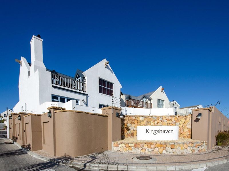 Front entrance view of Kingshaven townhouse complex featuring stone masonry, white facade, and secure boundary wall with electric fencing.