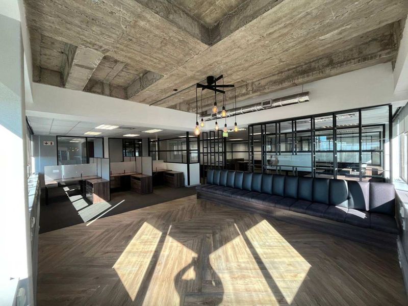 Modern open-plan office space featuring exposed concrete ceilings, herringbone wood flooring, built-in bench seating, and contemporary glass partition walls.