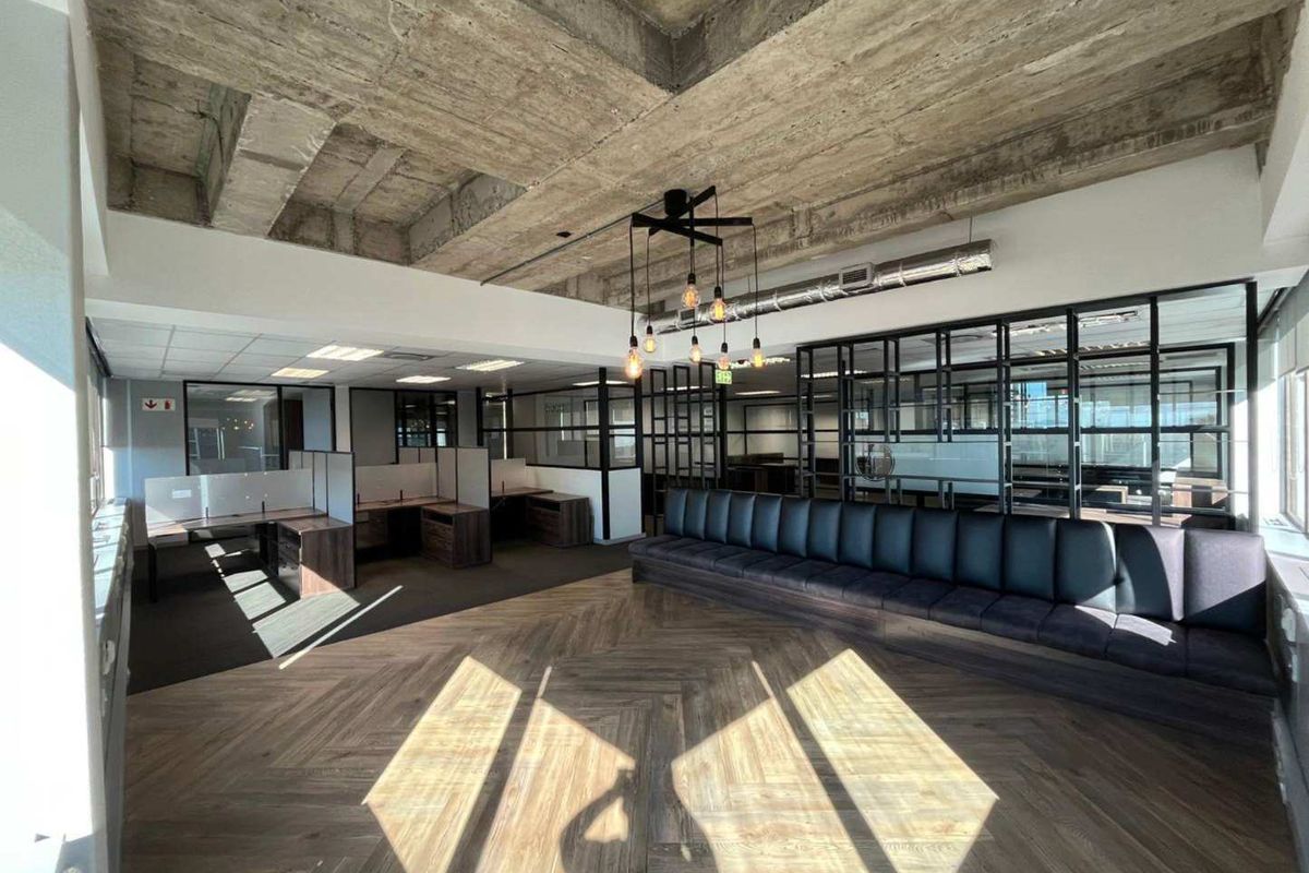 Modern open-plan office space featuring exposed concrete ceilings, herringbone wood flooring, built-in bench seating, and contemporary glass partition walls.