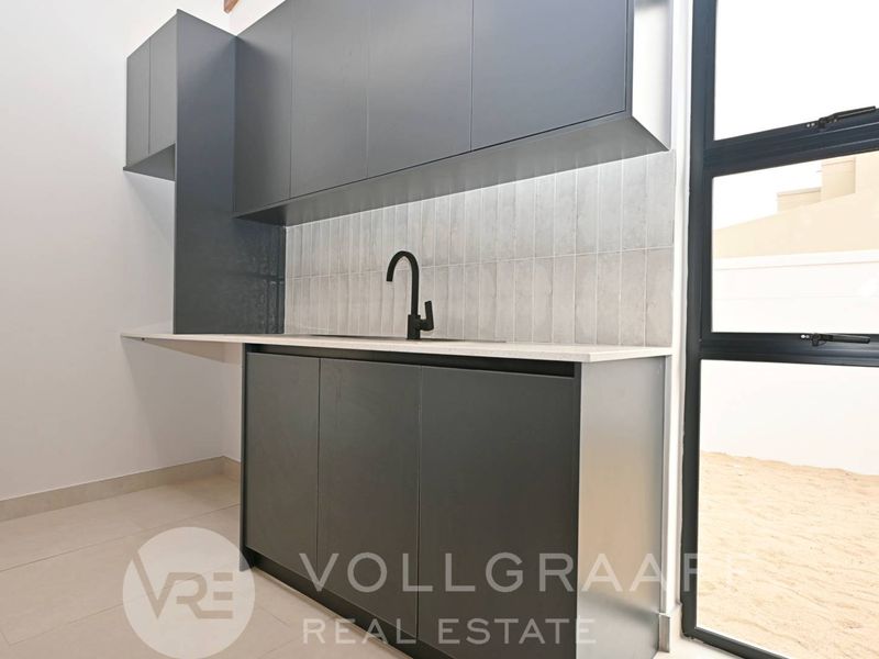 Modern scullery featuring sleek dark cabinetry, stone countertops, a contemporary black mixer tap, and a tiled backsplash with direct access to the exterior.