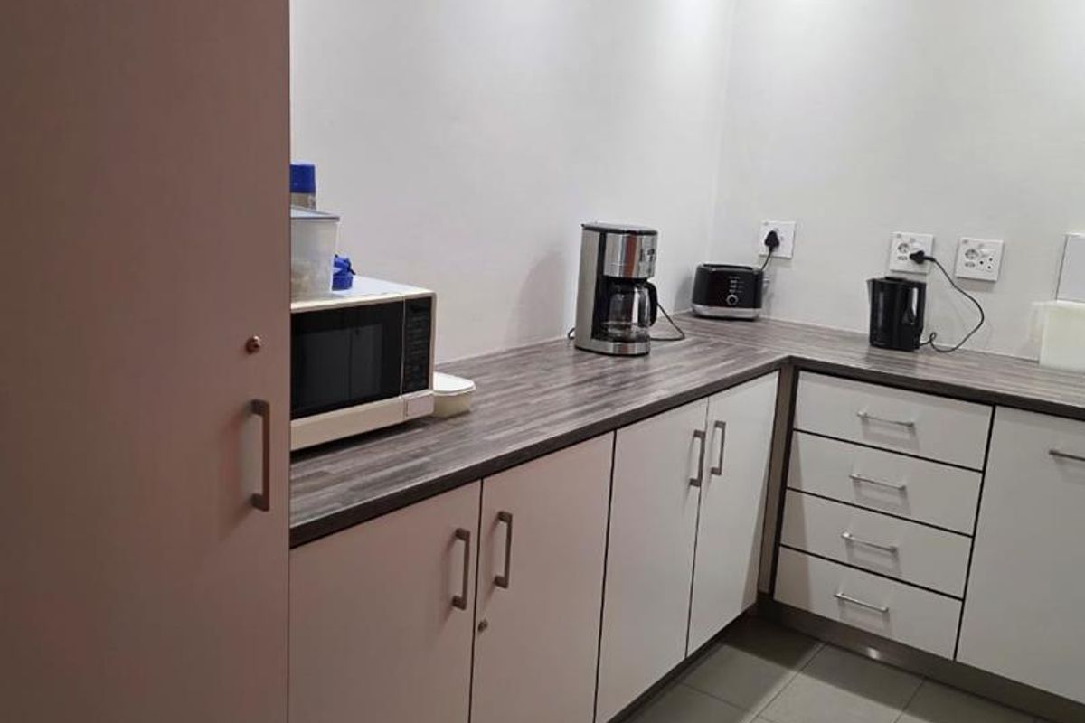 A functional kitchenette area featuring white cabinetry, dark wood-look laminate countertops, and tiled flooring, suitable for office or industrial utility use.