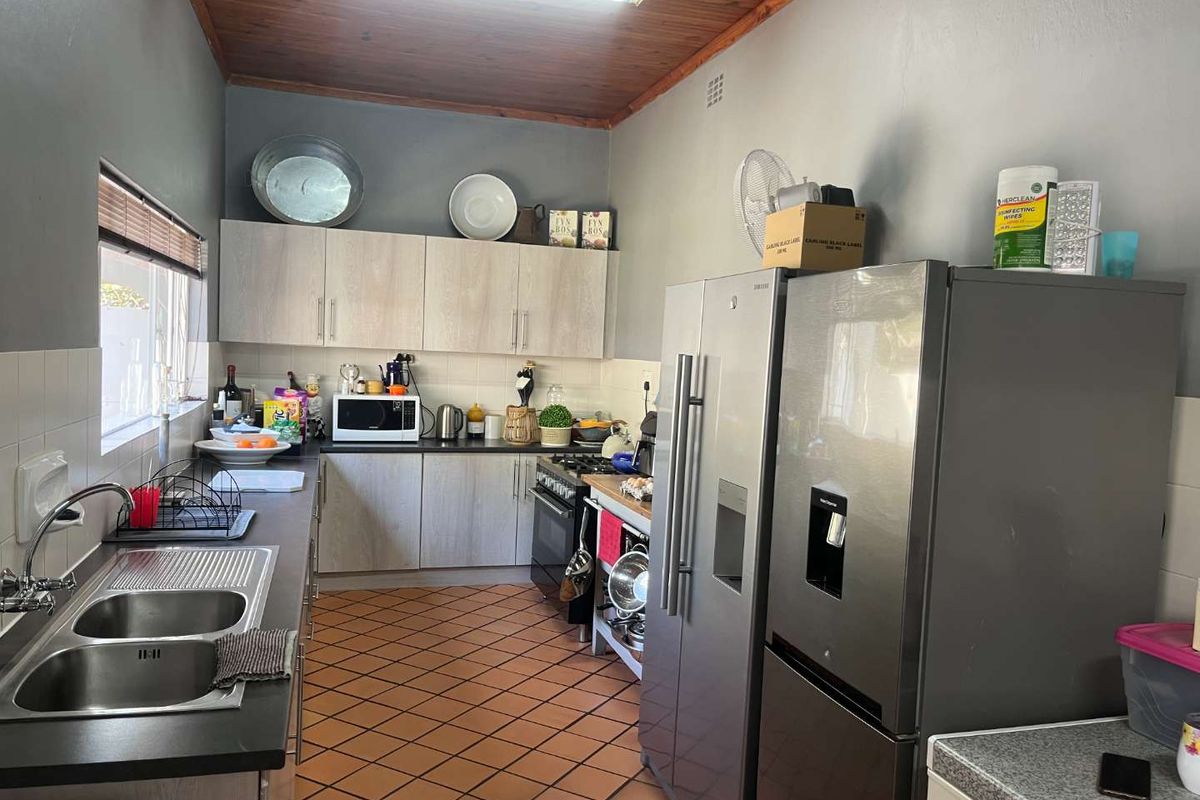 Functional kitchen featuring light-toned cabinetry, dark countertops, double stainless steel sink, and a gas stove, finished with terracotta floor tiles and a timber ceiling.
