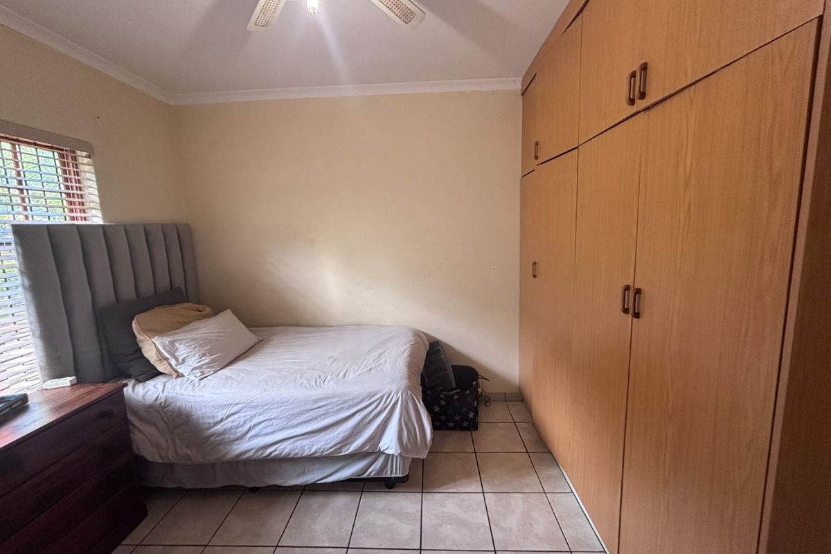 A bedroom featuring built-in wooden cupboards, tiled flooring, and a ceiling fan, offering functional storage space.