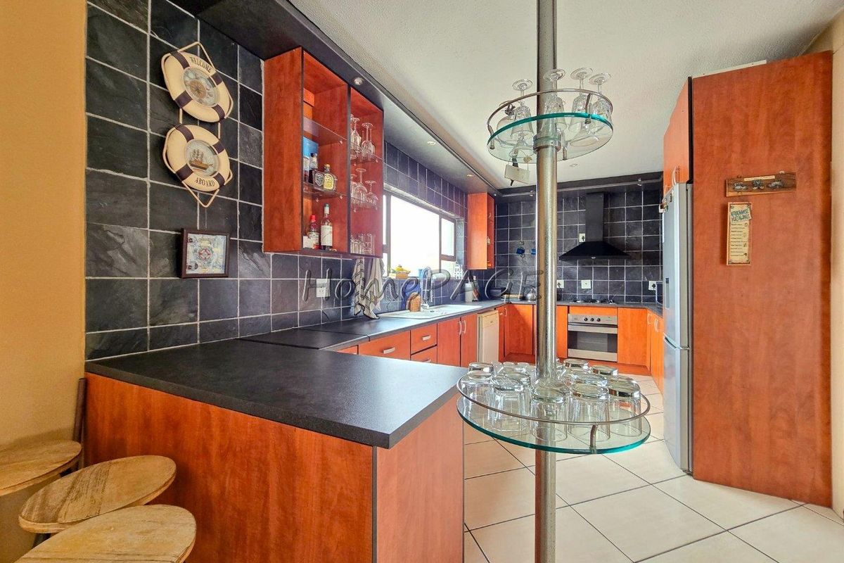 A functional kitchen featuring wood-finish cabinetry, dark tiled backsplash, built-in oven with extractor fan, and a central glass-topped breakfast bar.