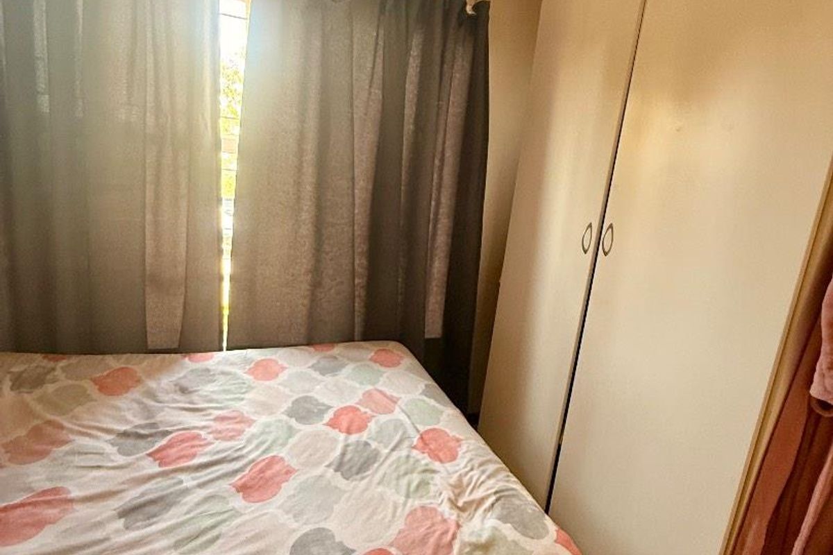 A bedroom featuring built-in cupboards and tiled flooring, with natural light entering through the window.