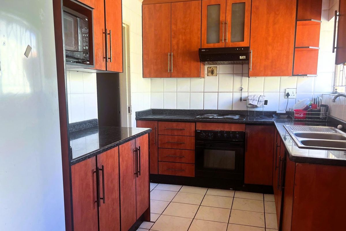 A functional kitchen featuring wood-finish cabinetry, dark granite countertops, a built-in oven, hob, and extractor fan with tiled flooring.