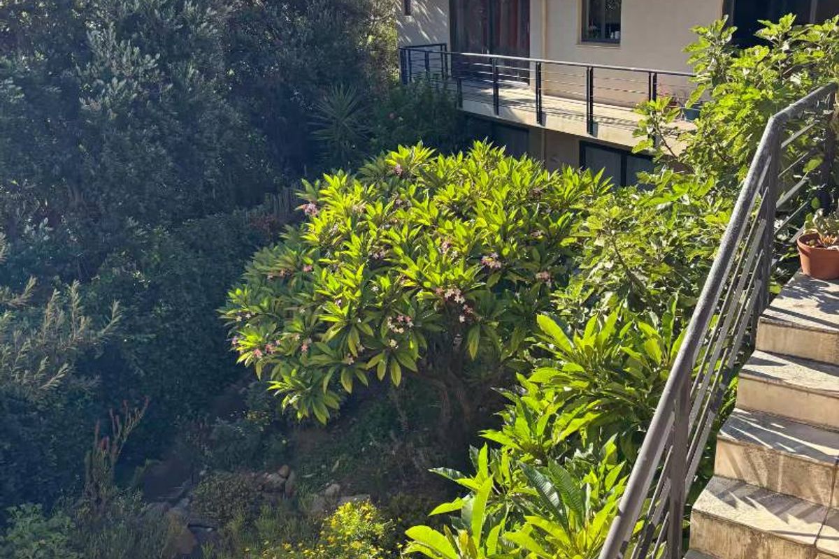 A view of the rear exterior of the house, featuring multi-level balconies, metal railings, and a lush, landscaped garden with mountain views.
