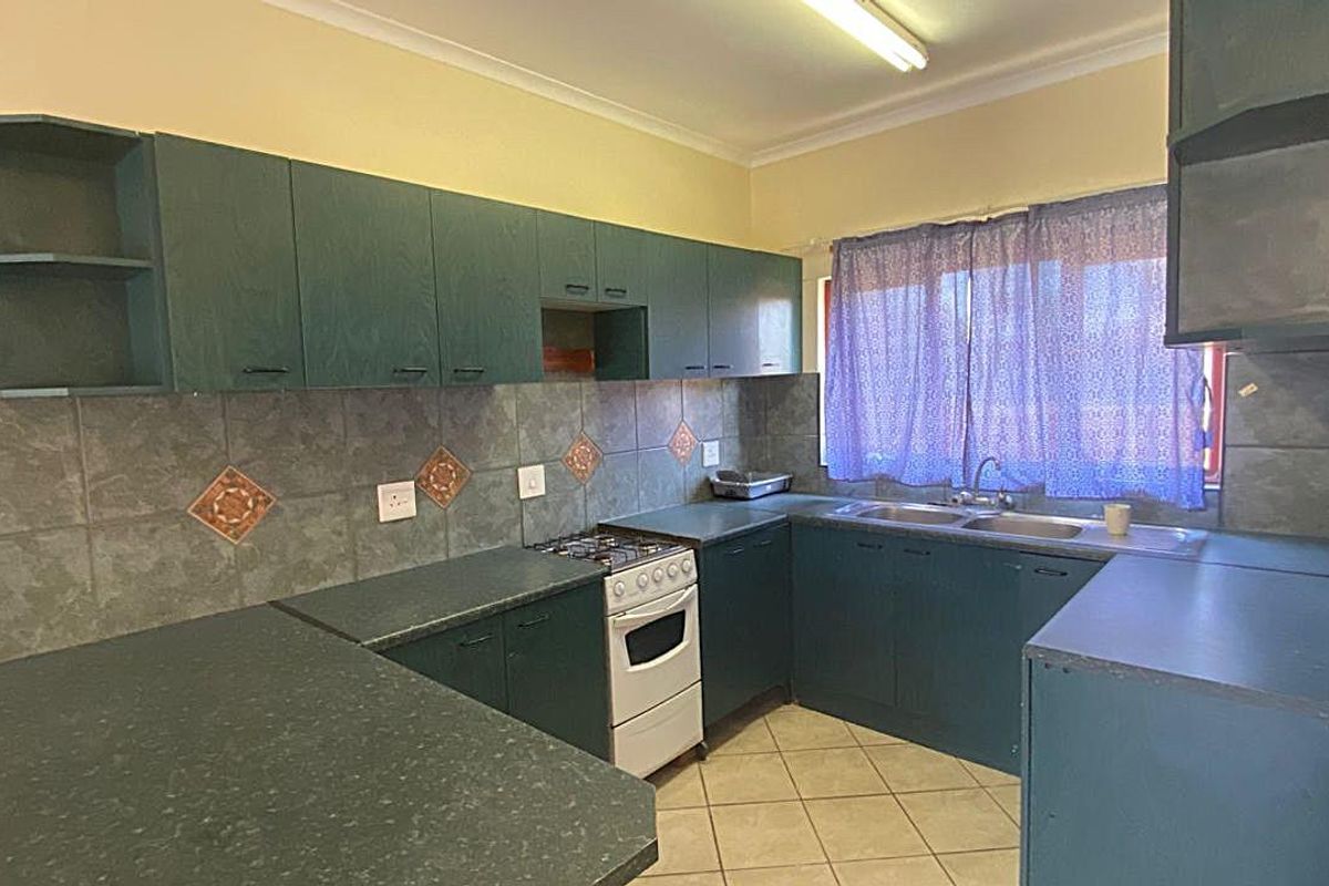 A functional kitchen featuring dark green cabinetry, tiled splashbacks, a built-in stove, and a double-basin sink with ample counter space.