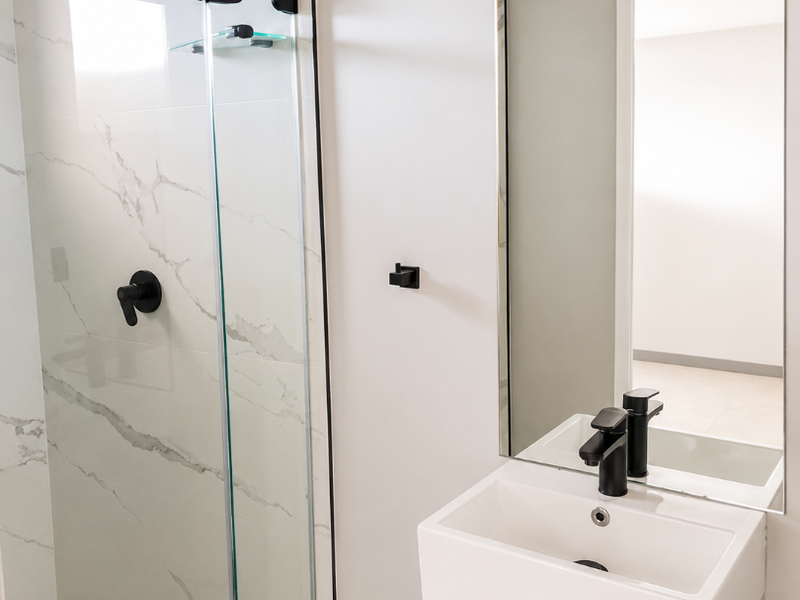 Modern bathroom featuring a glass-enclosed shower with marble-look tiling, a sleek vanity basin, and contemporary black fixtures.