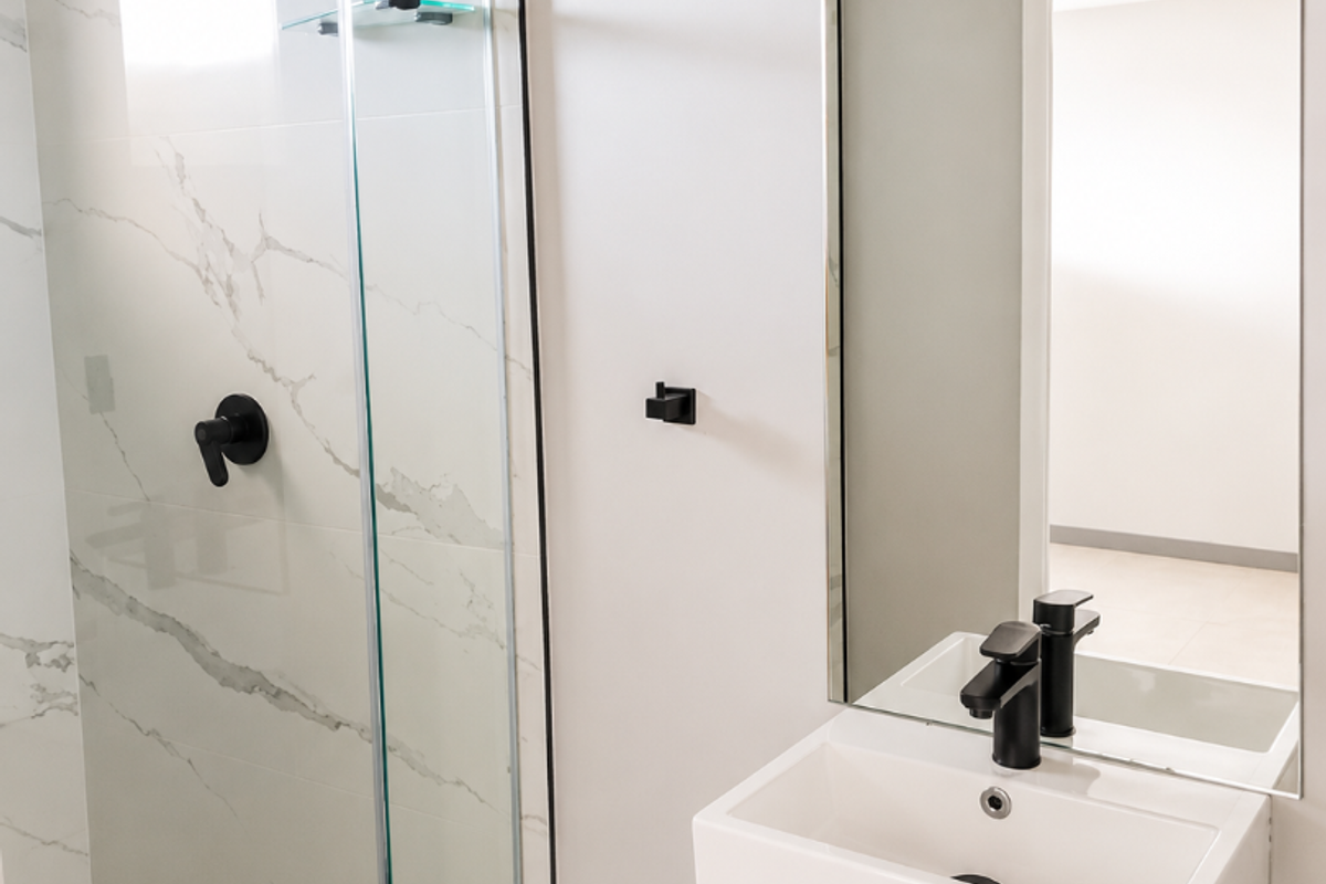 Modern bathroom featuring a glass-enclosed shower with marble-look tiling, a sleek vanity basin, and contemporary black fixtures.