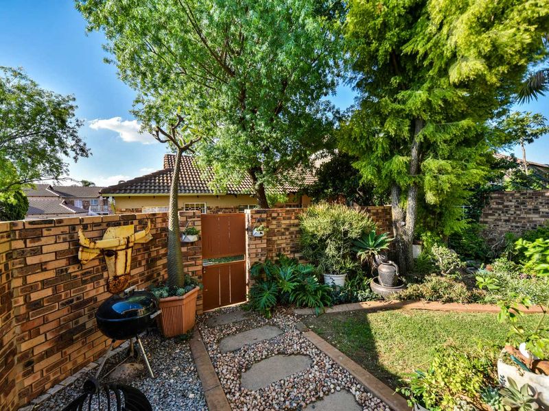 A well-maintained private garden featuring a brick boundary wall, a pedestrian gate, and a stone pathway leading through established greenery.