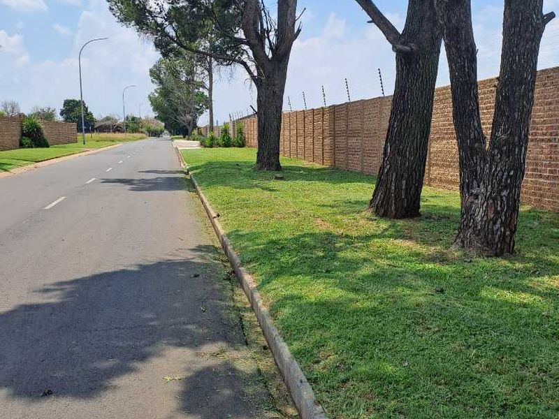 A view of the street frontage featuring a well-maintained brick boundary wall with electric fencing, mature trees, and a paved road.
