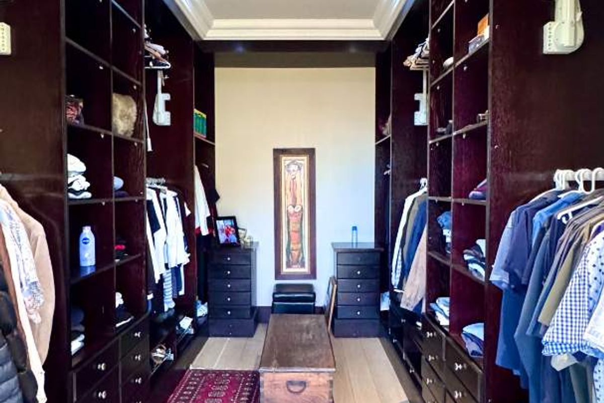 A spacious walk-in closet featuring extensive dark wood built-in cabinetry, recessed ceiling lighting, and light hardwood flooring.