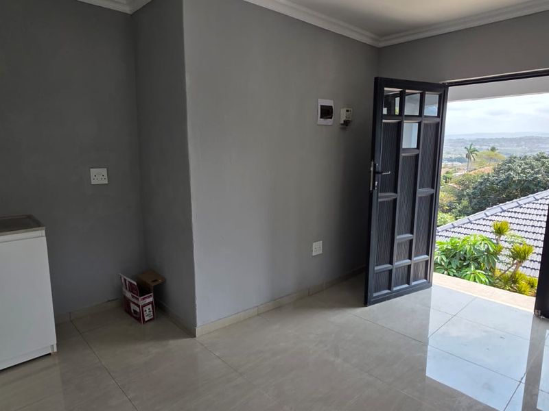 A compact, empty kitchen area featuring tiled floors, base cabinetry with a sink, and direct access to an outdoor balcony with scenic views.