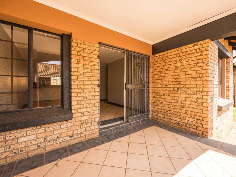 A covered patio area featuring face brick walls, tiled flooring, and a security gate, providing direct access to the interior of the townhouse.