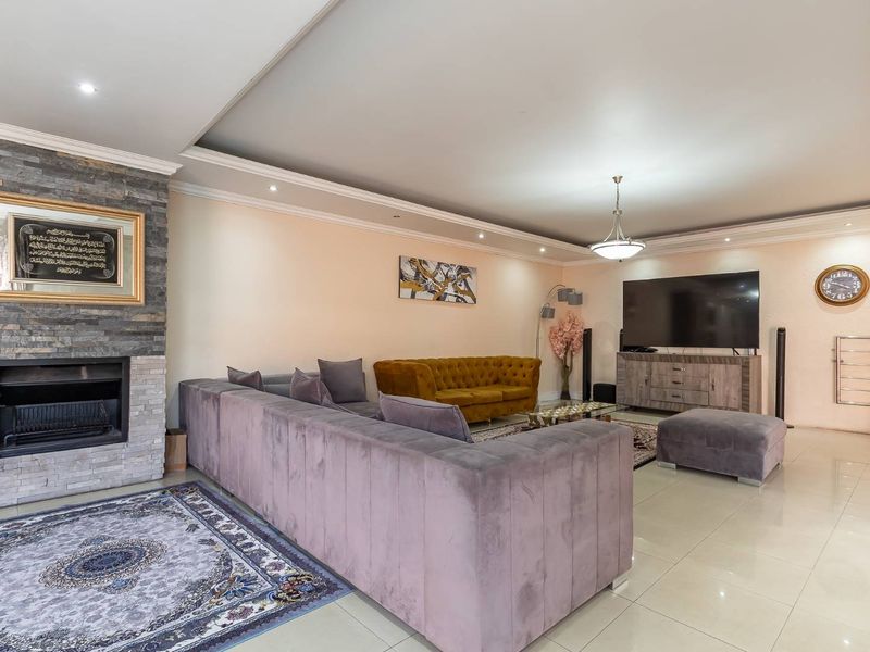 Spacious living room featuring a prominent stone-clad fireplace, recessed ceiling lighting, decorative cove molding, and polished tiled flooring.