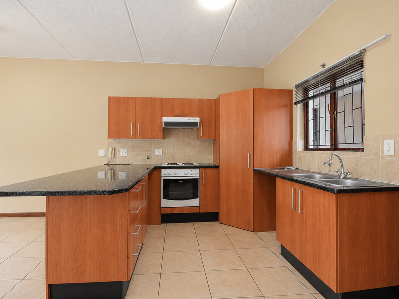 A functional kitchen featuring laminate cabinetry, granite countertops, built-in oven with hob, and a double bowl sink with tiled backsplash.